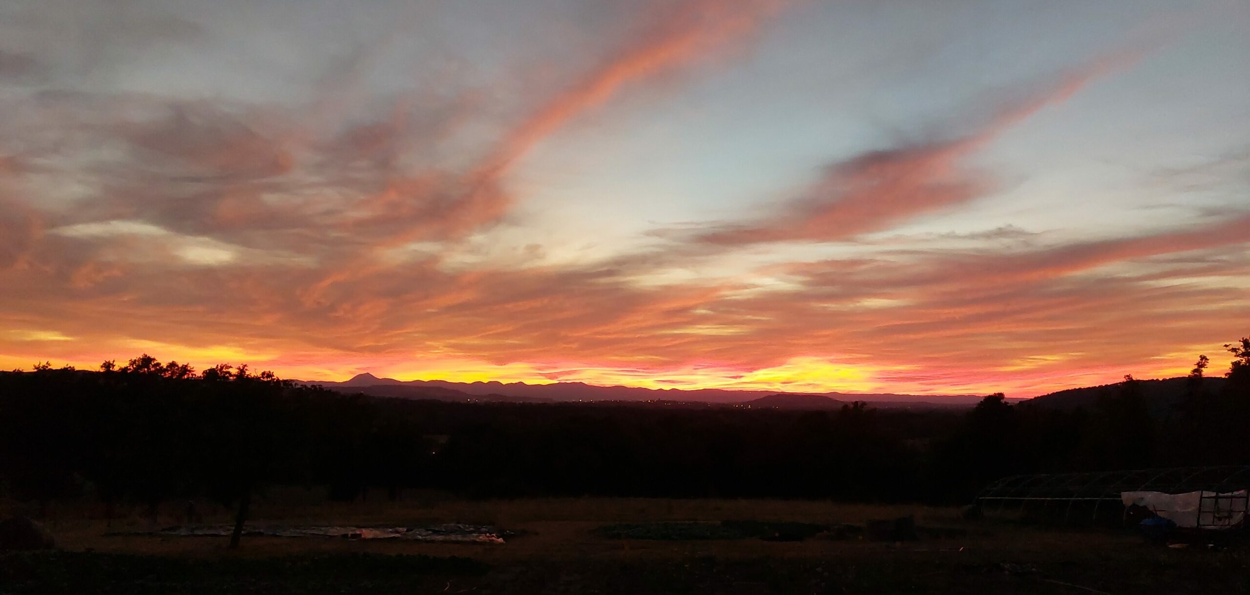Photo d'un ciel nuageux et rougeoyant, à l'horizon se découpe le Puy de Dôme et une partie de la chaîne des Puys.